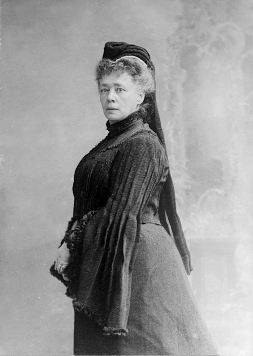 Schwarzweißfoto von Bertha von Suttner im dunklen Kleid mit Haube, stehend im Halbprofil