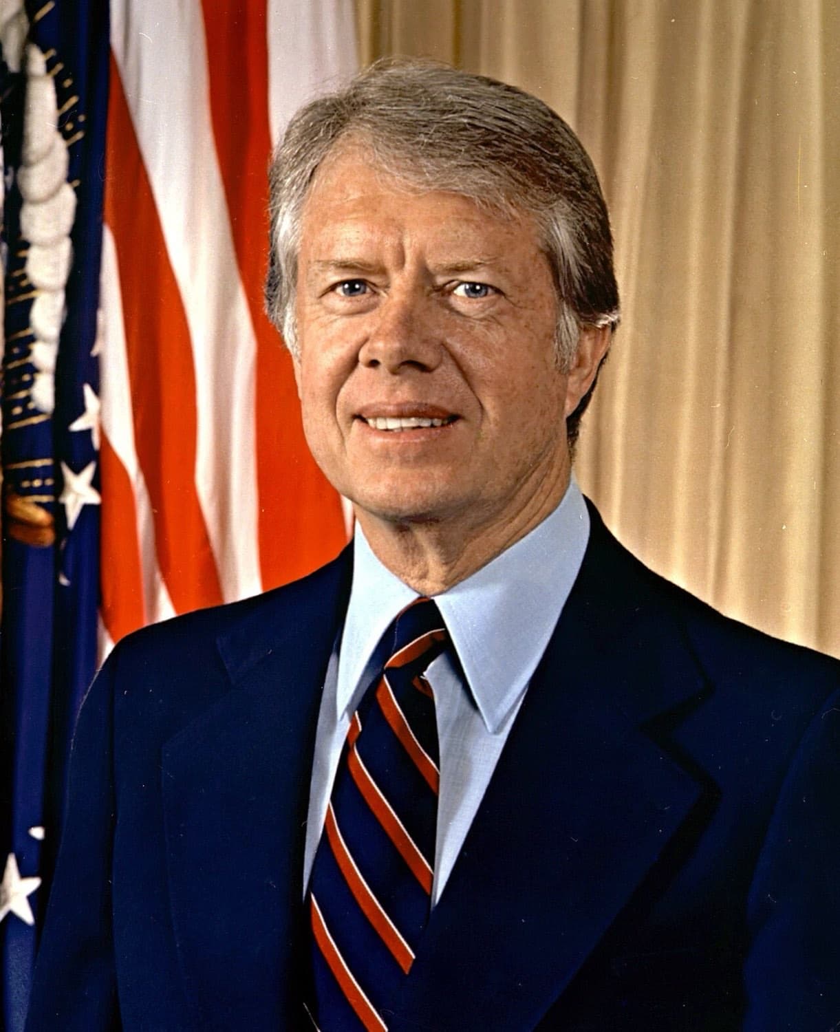 Jimmy Carter im dunklen Anzug mit gestreifter Krawatte vor einer amerikanischen Flagge