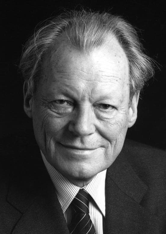 Schwarz-Weiß-Porträt von Willy Brandt im Anzug mit Krawatte, lächelnd vor dunklem Hintergrund
